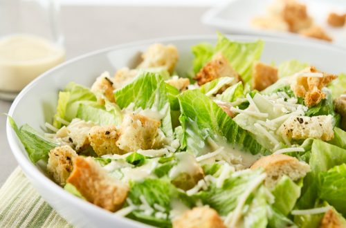 Closeup of a fresh caesar salad, with romaine lettuce hearts, croutons, parmesan cheese and dressing. Dressing and croutons in background. Very shallow DOF."