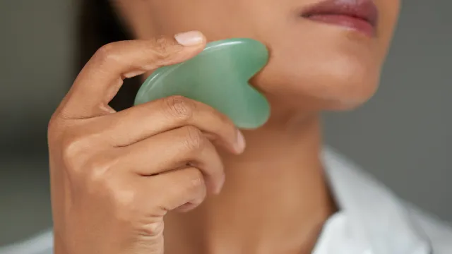 Close of up of woman using a jade green gua sha stone on her face