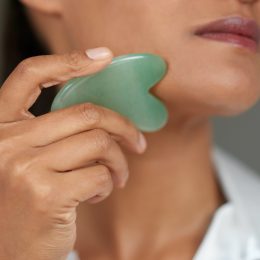 Close of up of woman using a jade green gua sha stone on her face