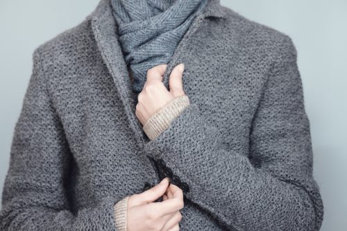 Closeup of a person in a gray wool coat with a gray scarf against a gray background