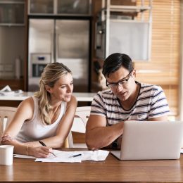 A couple sitting at their kitchen table going over their budget or taxes with a laptop and papers