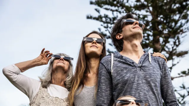 A family with four people look at a solar eclipse while wearing protective glasses