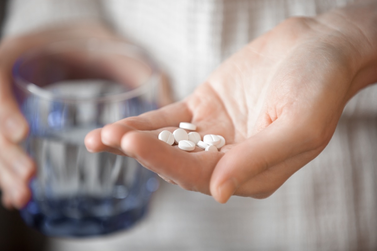 Healthcare, treatment, supplements concept photo. Woman arm holding heap of small round meds and glass of water before taking medication, shallow depth of field, focus on medicine