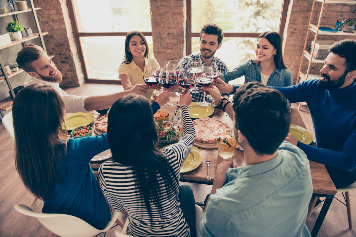 Group of friends sitting around a dinner table toasting with glasses of red wine