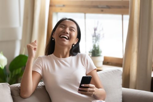woman laughing on couch while scrolling on her phone