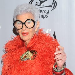 portrait of Iris Apfel wearing an orange fuzzy coat and large, round black glasses