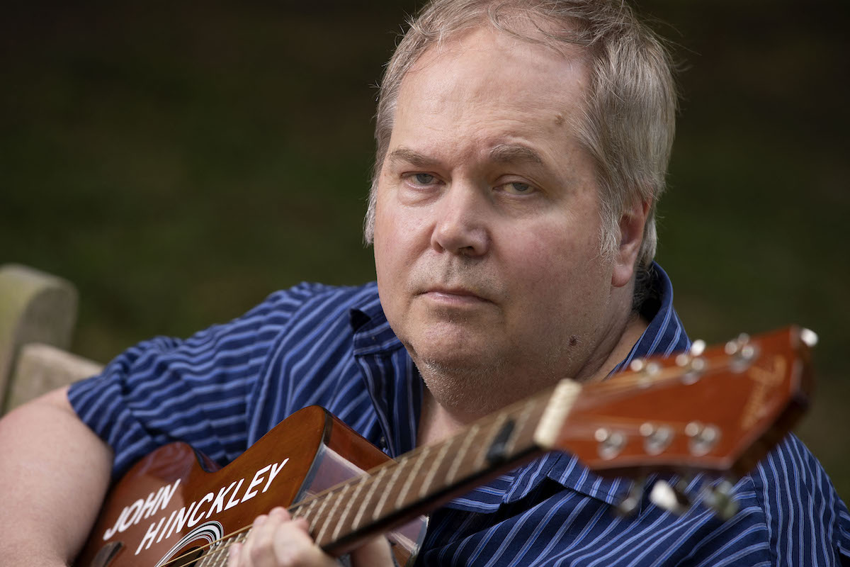 Portrait of John Hinckley Jr. holding his monogrammed guitar