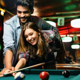 Portrait of young couple having fun playing billiard together. The man is showing the woman how to shoot pool.
