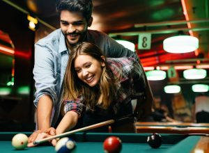 Portrait of young couple having fun playing billiard together. The man is showing the woman how to shoot pool.