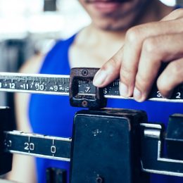 Sport man weighing himself on balance weight scale at the gym