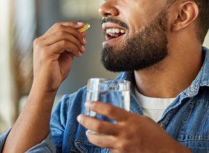 Close-up portrait of a man wearing a denim shirt taking a vitamin with a glass of water