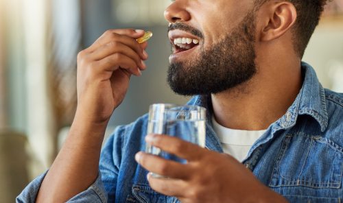 Close-up portrait of a man wearing a denim shirt taking a vitamin with a glass of water