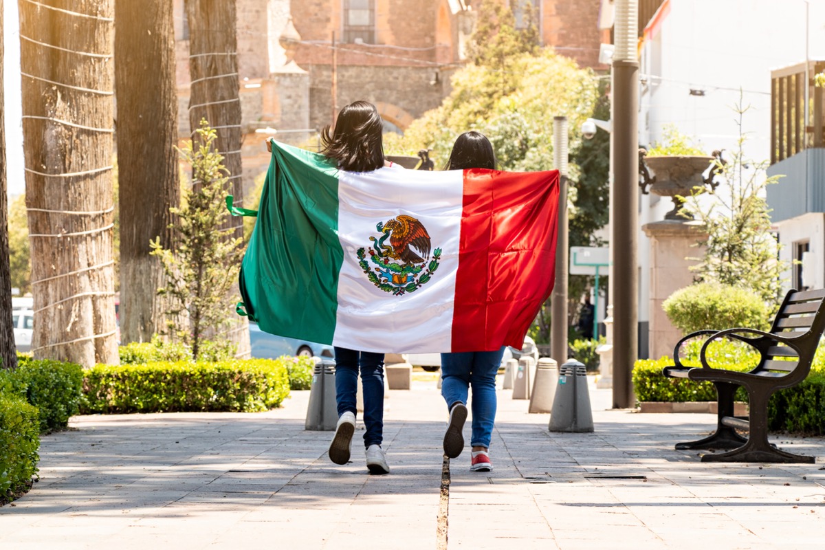 two young women running on a sidewalk with the mexican flag