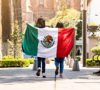 two young women running on a sidewalk with the mexican flag