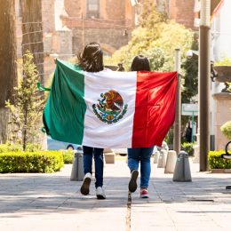 two young women running on a sidewalk with the mexican flag