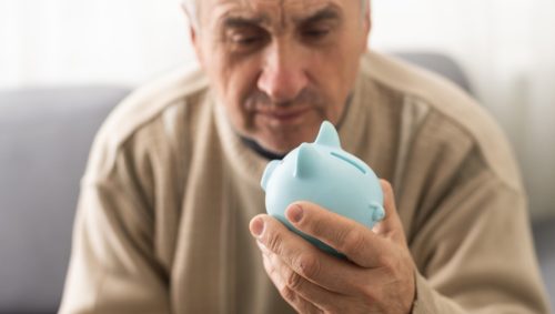 Senior man holding piggy bank with glasses depressed and worry for distress, crying angry and afraid. sad expression.