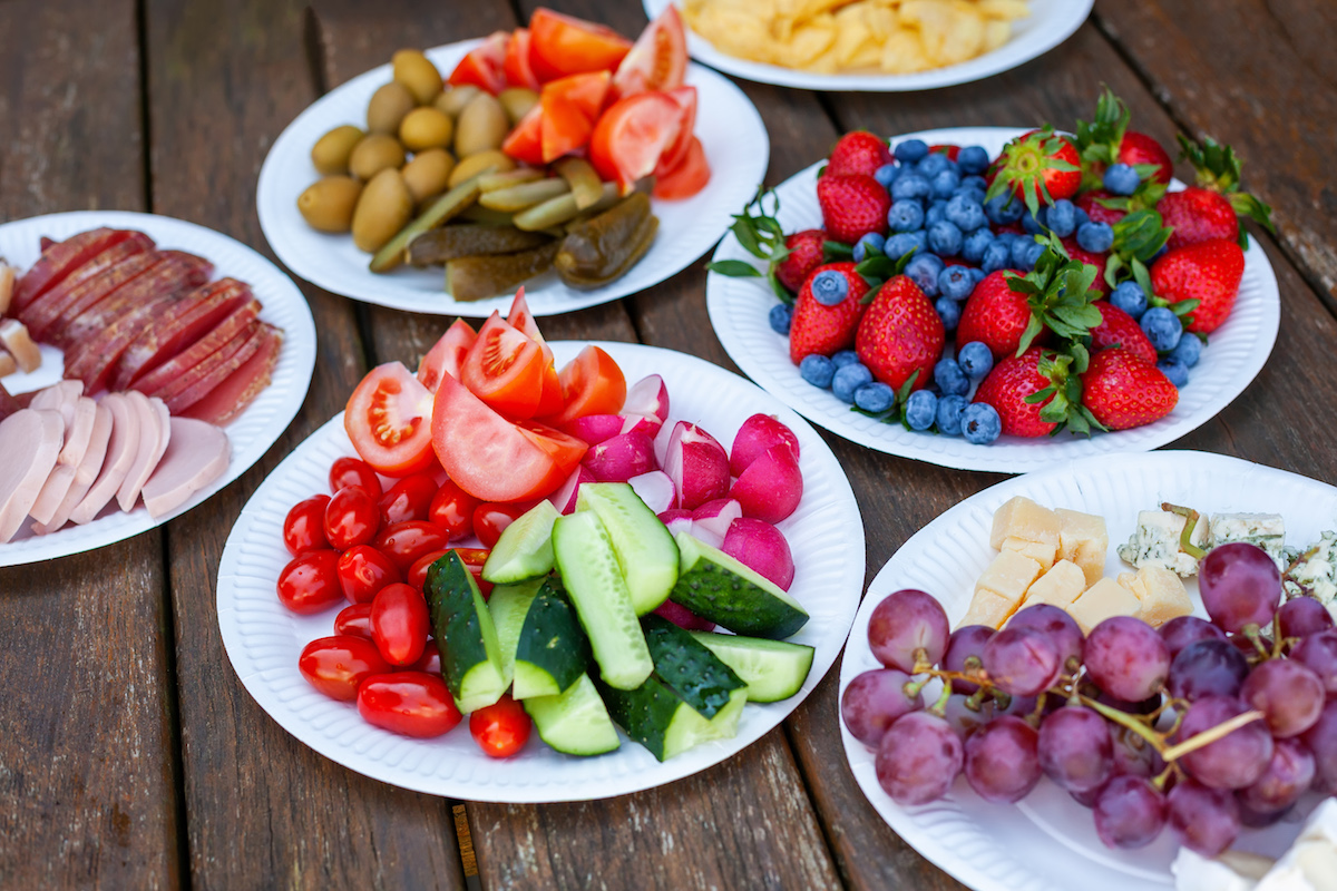 Variety of healthy party food and snacks on paper plates - fruits, vegetables and cheese