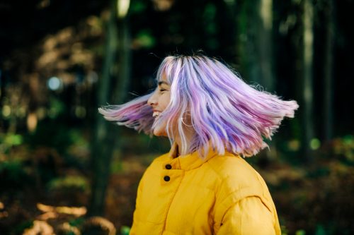 Portrait of confident, young, modern teenage girl with pink, blue hair in nature forest, Germany