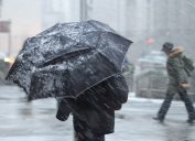 A pedestrian walking in a snowstorm with an umbrella