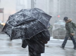 A pedestrian walking in a snowstorm with an umbrella