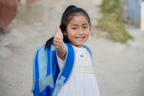 little girl with a backpack on making a thumbs up at the camera