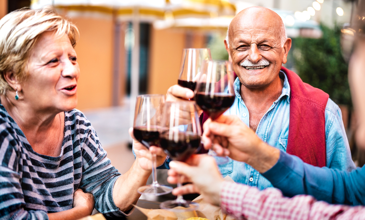 Happy senior couple having fun drinking red wine with friends at dinner party