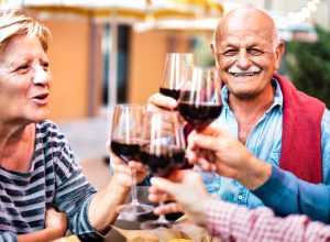 Happy senior couple having fun drinking red wine with friends at dinner party