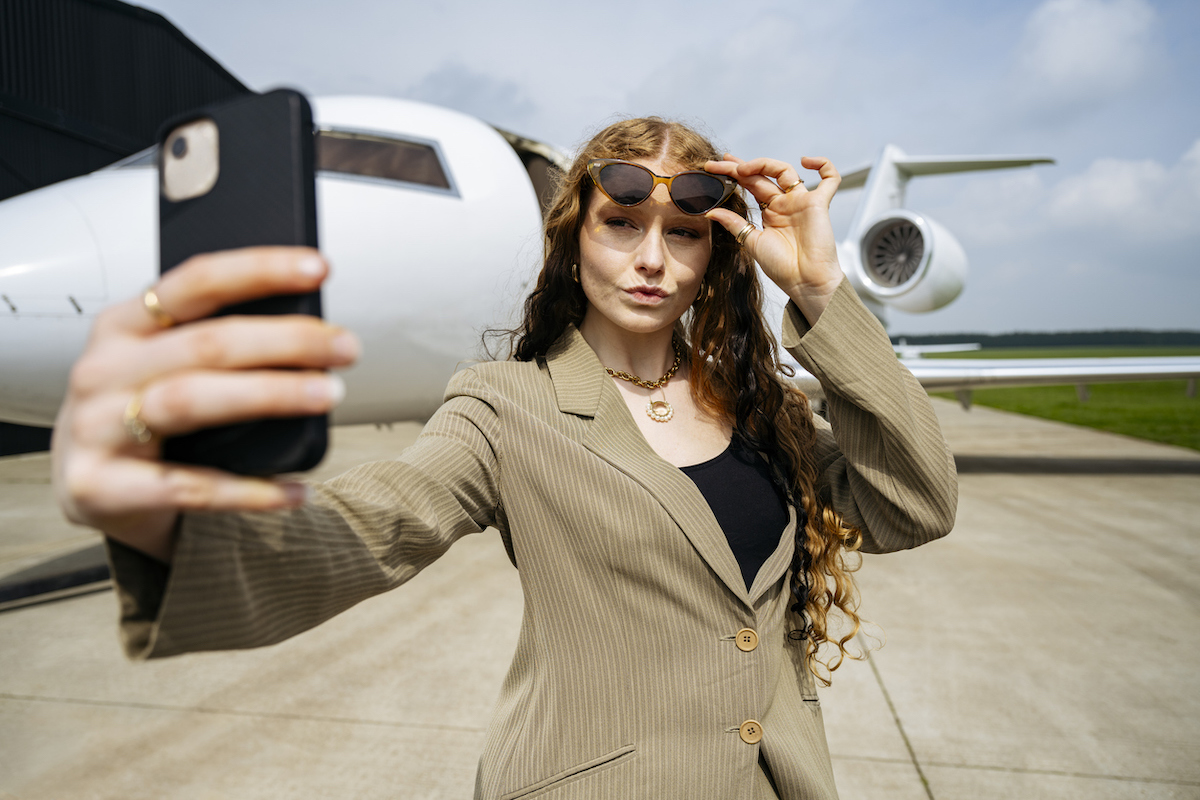 snobby-looking businesswoman taking a selfie in front of a private jet