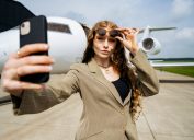 snobby-looking businesswoman taking a selfie in front of a private jet