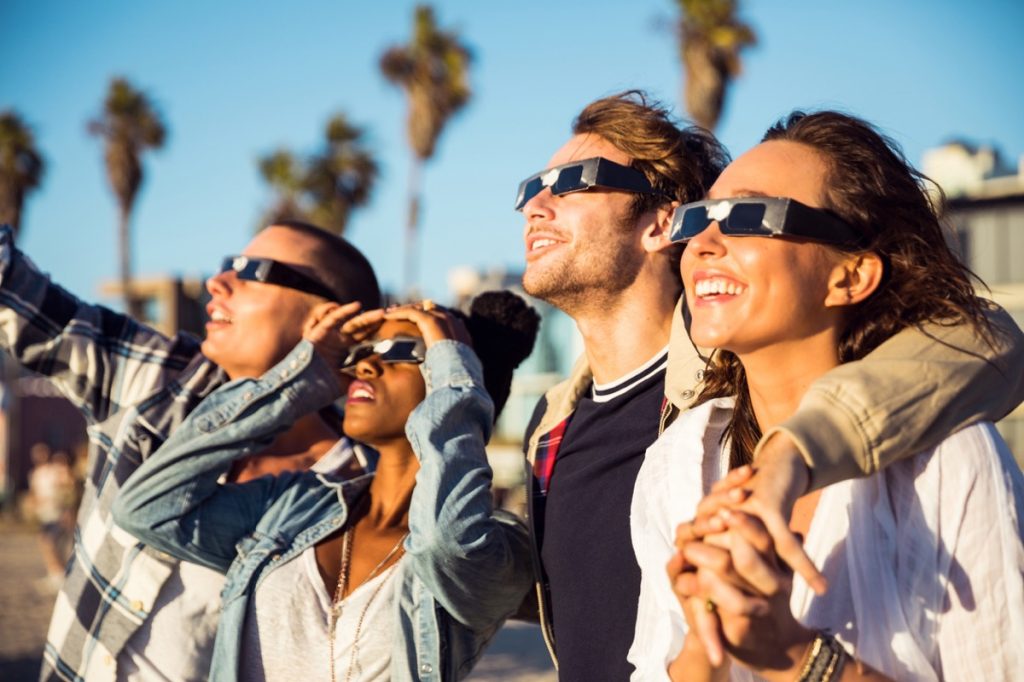 A group of four friends watching a solar eclipse with protective glasses on