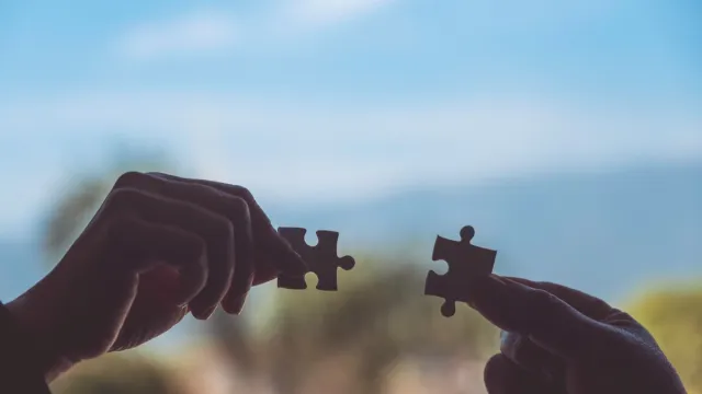 Closeup image of two hands holding jigsaw puzzle pieces together