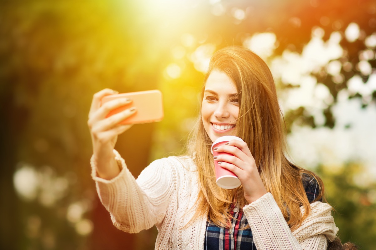 woman taking a selfie and holding a takeout coffee cup in spring time