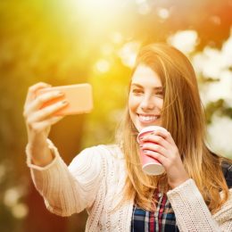 woman taking a selfie and holding a takeout coffee cup in spring time