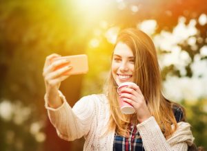 woman taking a selfie and holding a takeout coffee cup in spring time