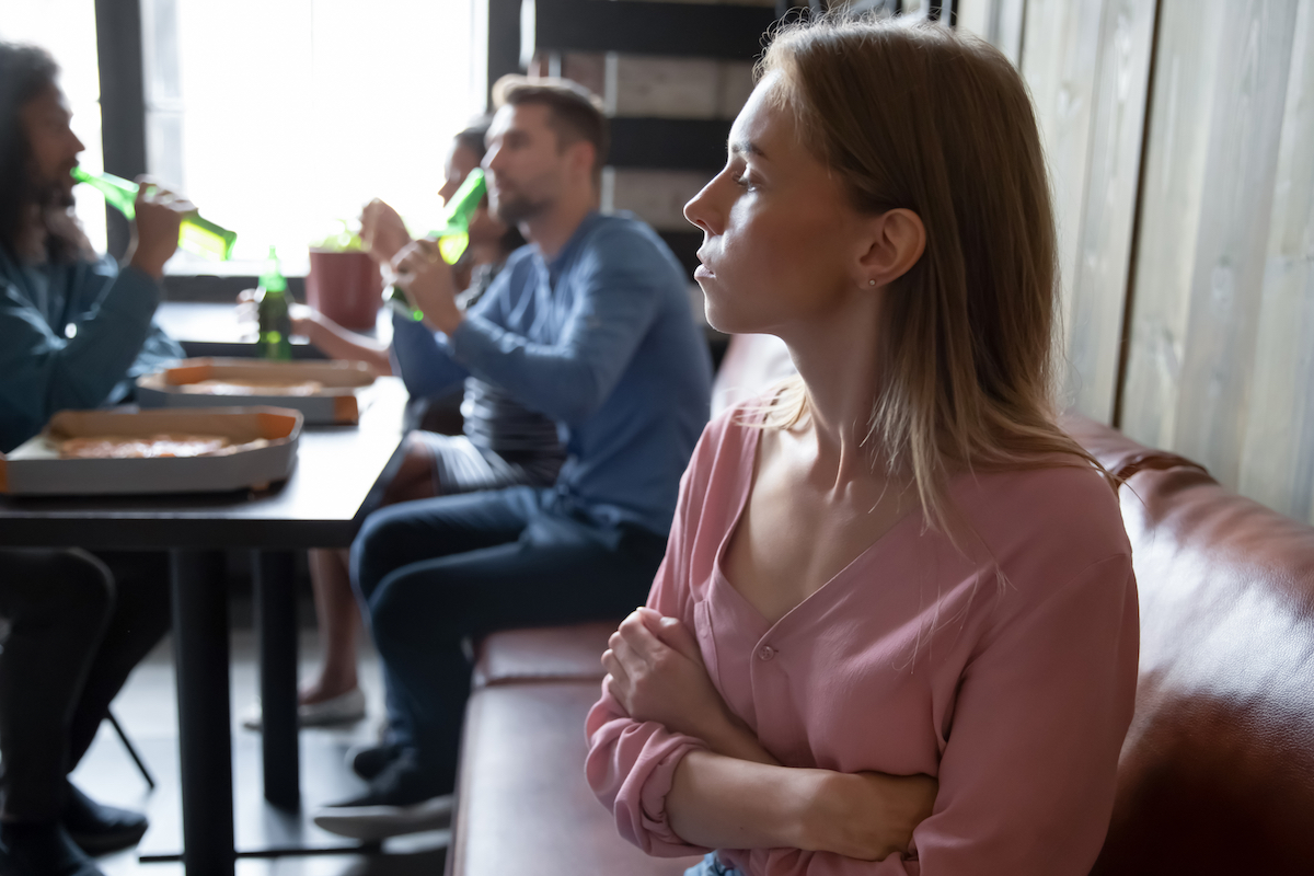 Upset offended young woman sitting separately from friends in cafe
