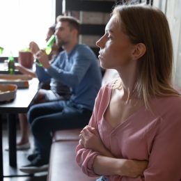 Upset offended young woman sitting separately from friends in cafe