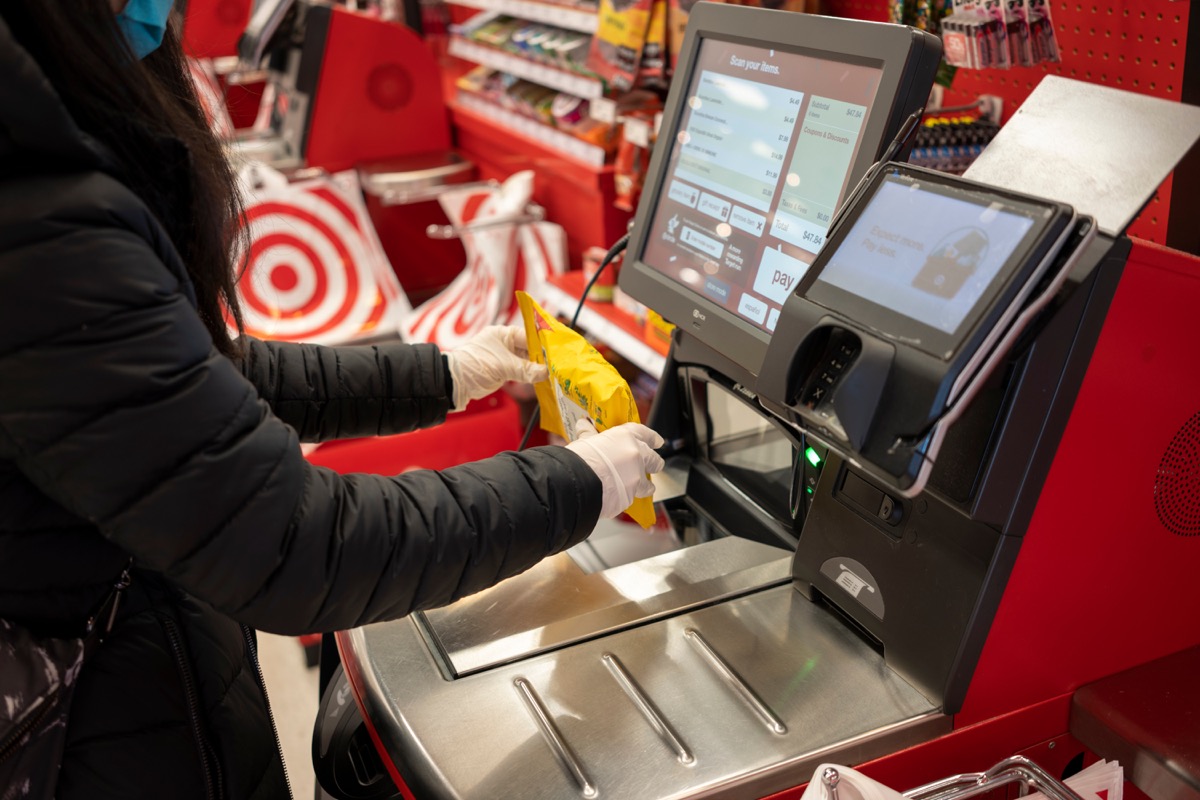 Tigard, OR, USA - Feb 21, 2021: A masked shopper in nitrile gloves scans a bag of Ricola cough drops at the self-checkout lane in a Target store in Tigard, Oregon.