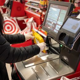 Tigard, OR, USA - Feb 21, 2021: A masked shopper in nitrile gloves scans a bag of Ricola cough drops at the self-checkout lane in a Target store in Tigard, Oregon.