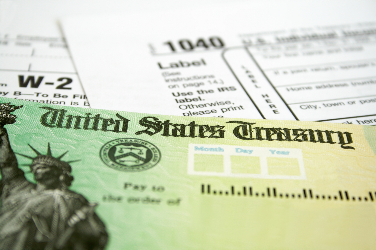 A close up of a tax refund check next to a 1040 form and a W-2