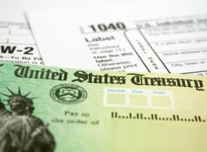 A close up of a tax refund check next to a 1040 form and a W-2