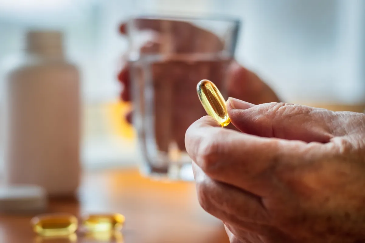Close up of a person's hands holding omega-3 fish oil nutritional supplement and glass of water