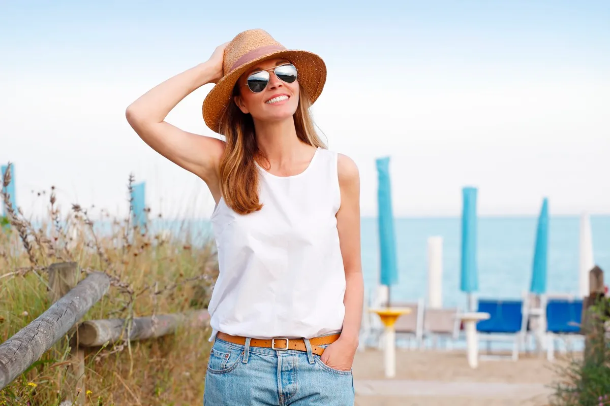 woman in a hat and sunglasses looking happy on a deck