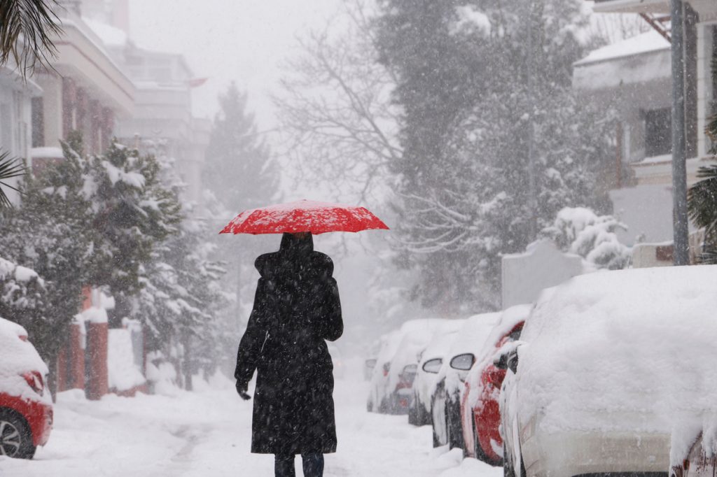 A person walking in a snowstorm in a city with a red umbrella