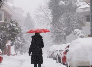 A person walking in a snowstorm in a city with a red umbrella