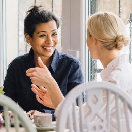 Two smiling women are sitting at a table in a cafe, socialising over tea.