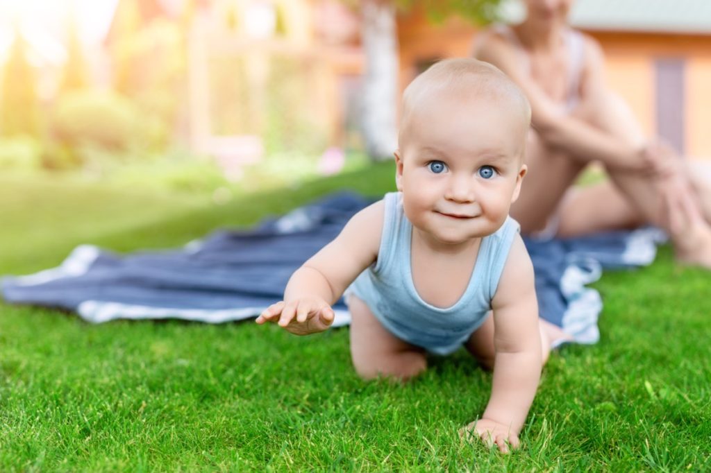 Baby crawling on grass with mother in the background