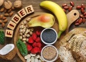 Foods rich in fiber as rye bread, wheat bran, white beans, red beans, spinach, almonds, poppy seed, pears, bananas, coconut, raspberries, pistachios, walnuts. Wooden table as background