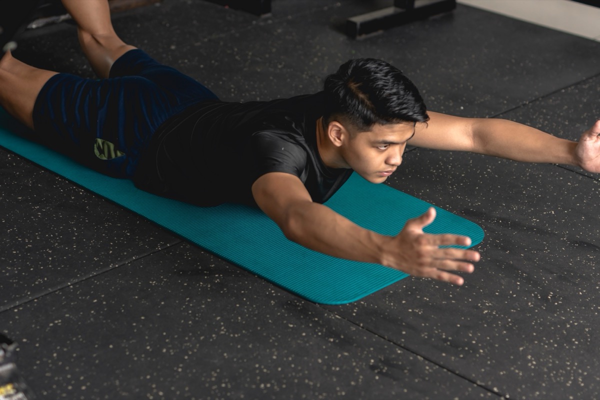A young handsome asian man does superman back extension exercises while lying prone on a mat at the gym. Training and strengthening lower back muscles.