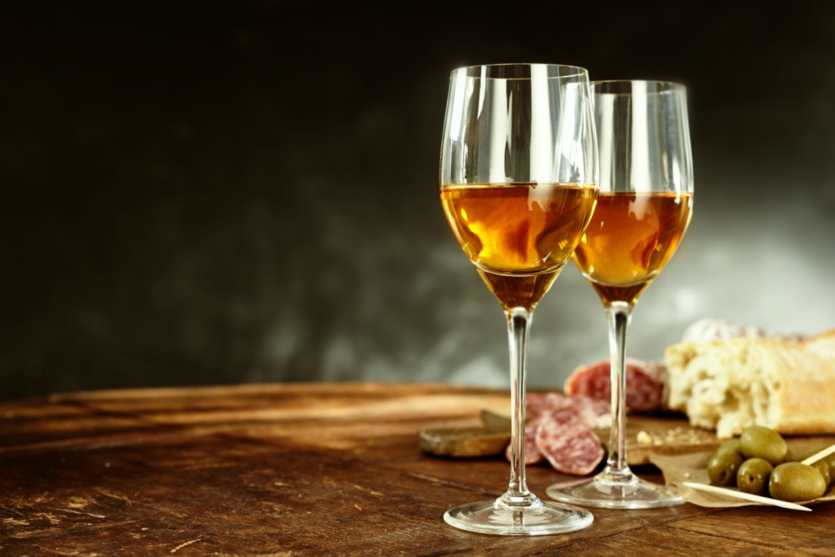 Two glasses of sherry served with tasty traditional Spanish tapas of olives, salami and fresh bread on an old wooden table