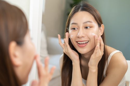 smiling young woman applying moisturizer for skincare routine